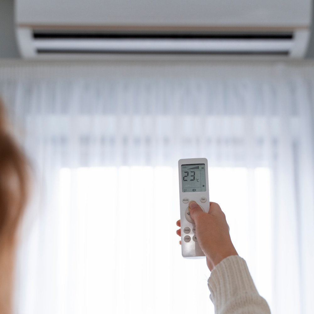 Eine Hand hält eine Klimaanlagen-Fernbedienung und zeigt auf die Inneneinheit.