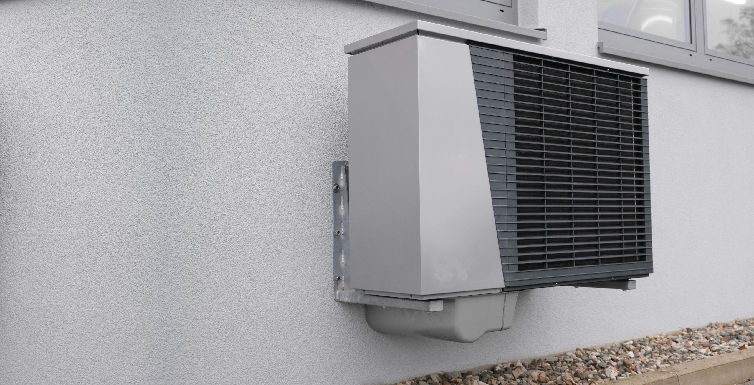 Eine an der Wand befestigte Außeneinheit einer Wärmepumpe, die Energieeffizienz und Kosteneinsparungen zeigt.