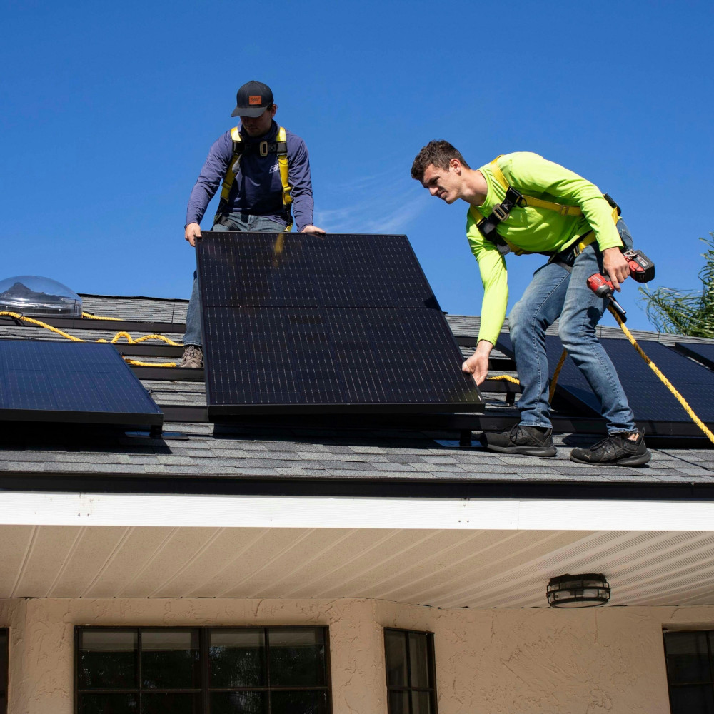 Zwei Männer installieren eine Solarthermieanlage auf einem Dach – einer hält eine Bohrmaschine, der andere stützt das Solarpanel.
