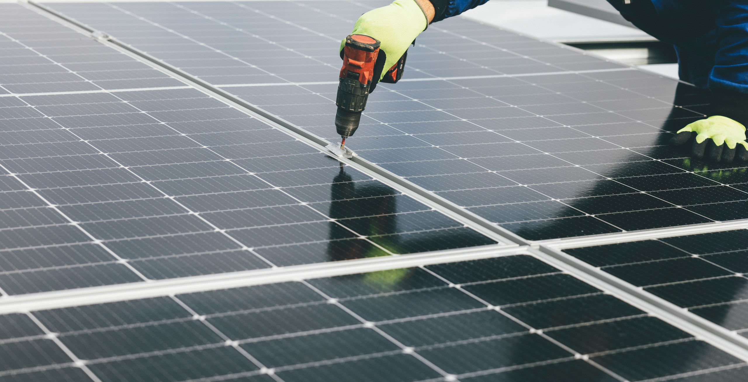 Makroaufnahme einer Hand mit einem Akkuschrauber, die eine Schraube befestigt, um ein Solarheizungsmodul auf dem Dach zu montieren.